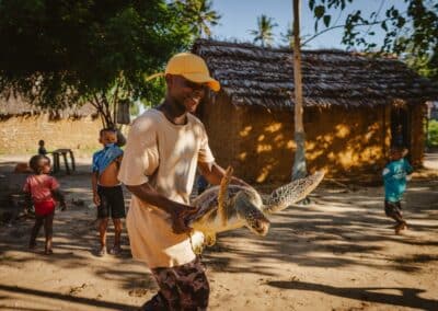 A man carries a turtle. Several children stand behind.