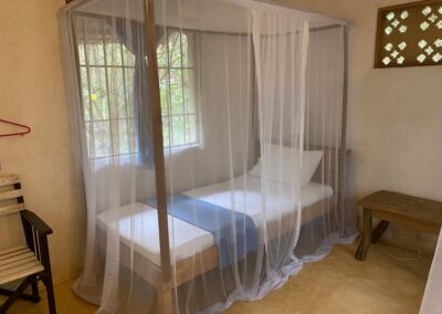 A bed surrounded by mosquito netting near a window.